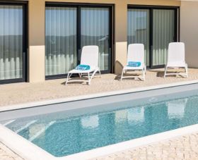 Blue swimming pool and sun chairs on a natural stone pavement outside a moder property built by Presprop and sold by Immo Portugal